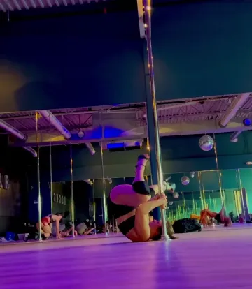 Dancer Rolls and Inverts by a Pole on a Purple-Lit Floor