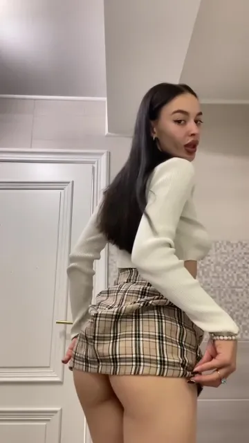 Brunette Lifts a Plaid Skirt in a Tiled Room