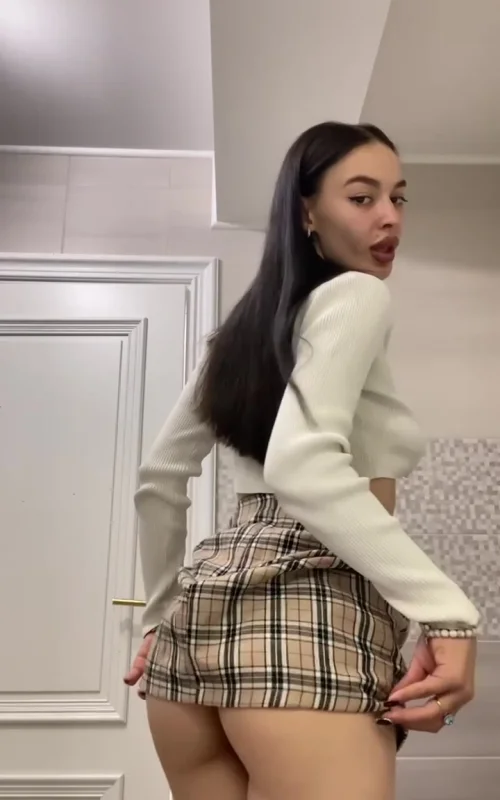 Brunette Lifts a Plaid Skirt in a Tiled Room